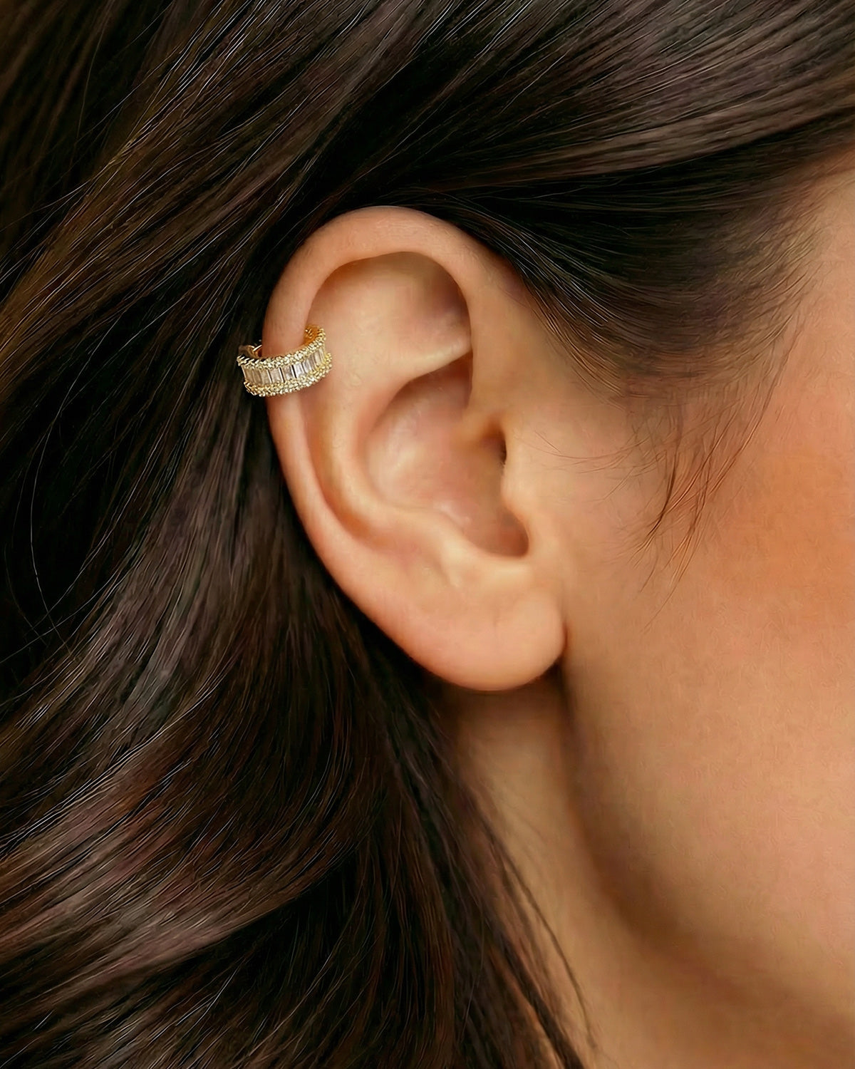 Altın renkli dikdörtgen zirkon taşlı halka piercingin helix ve kıkırdak bölgesinde duruşu.