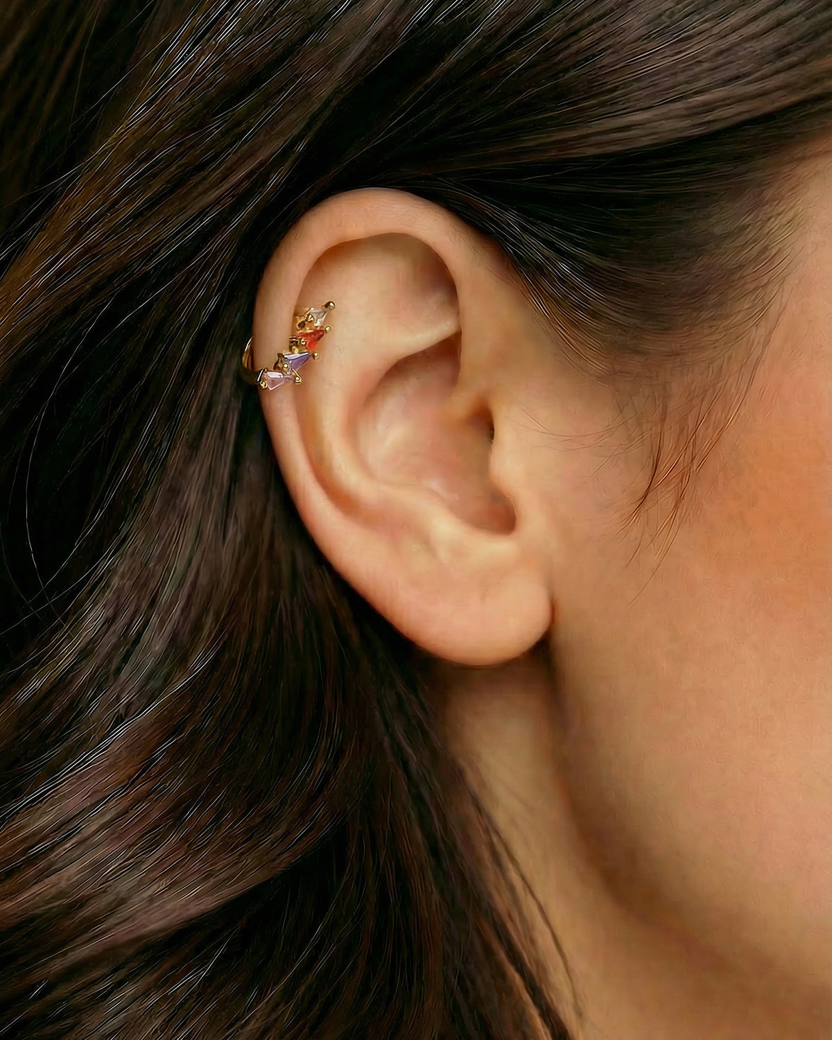 Altın renkli geometrik renkli zirkon taşlı halka piercingin helix ve kıkırdak bölgesinde duruşu.