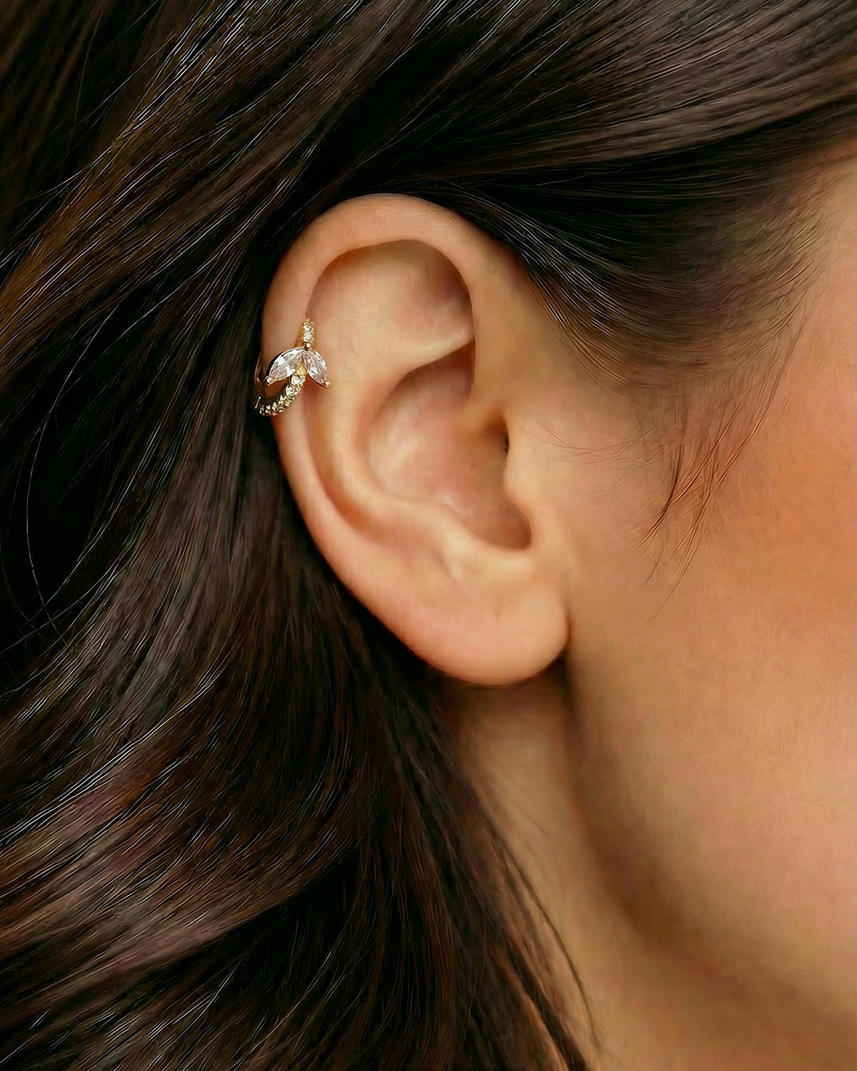 Altın renkli kanat formlu zirkon taşlı halka piercingin helix ve kıkırdak bölgesinde duruşu.