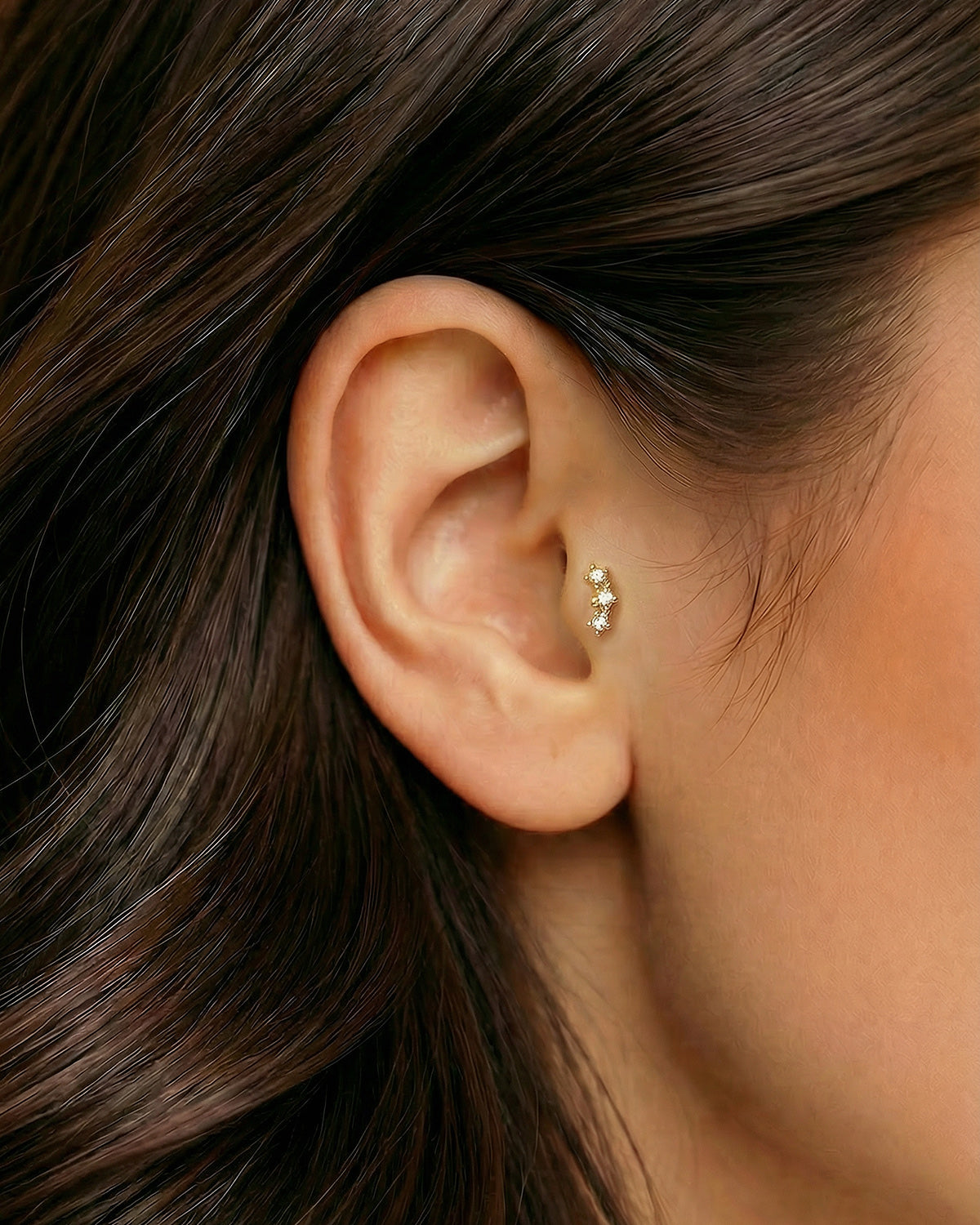 Altın renkli üçlü yıldız zirkon piercingin kulak kıvrımında ve tragusta duruşu.