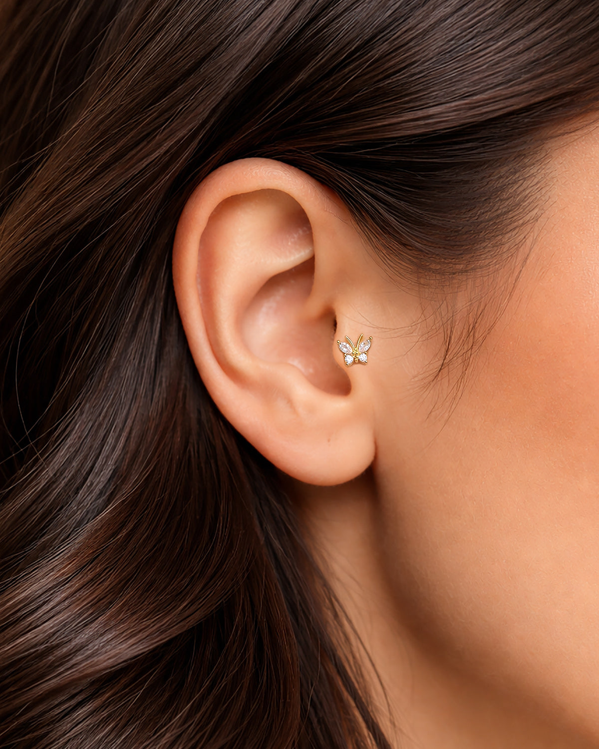 Altın renkli zirkon taşlı minimal kelebek piercingin tragus ve helixte duruşu.