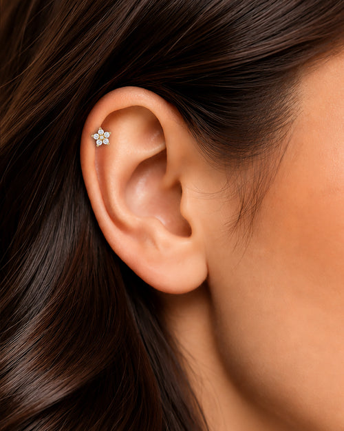 Altın renkli çiçek formlu flatback piercingin tragus ve helix bölgesindeki duruşu.