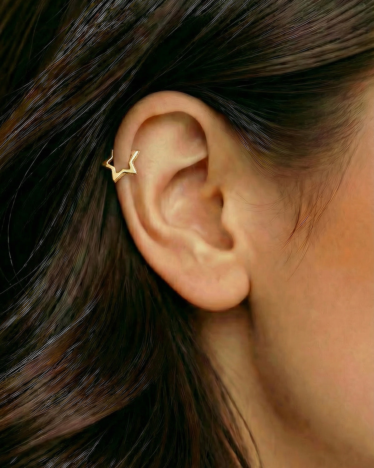 Altın renkli yıldız formlu zirkon taşlı halka piercingin helix ve kıkırdak bölgesinde duruşu.