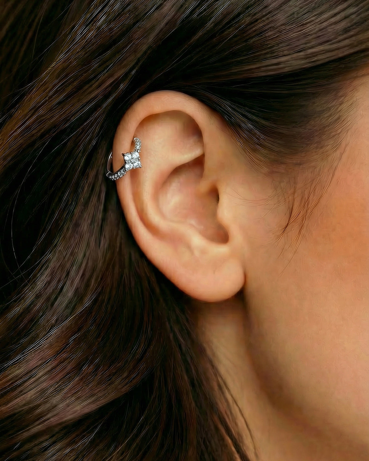 Gümüş renkli çiçek formlu dörtlü zirkon taşlı halka piercingin helix ve kıkırdak bölgesinde duruşu.