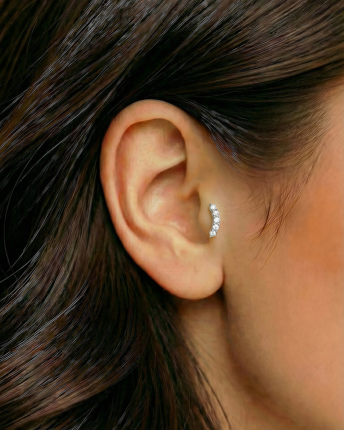 Gümüş renkli zirkon taşlı minimal kavisli piercingin tragus ve helix bölgesinde duruşu.