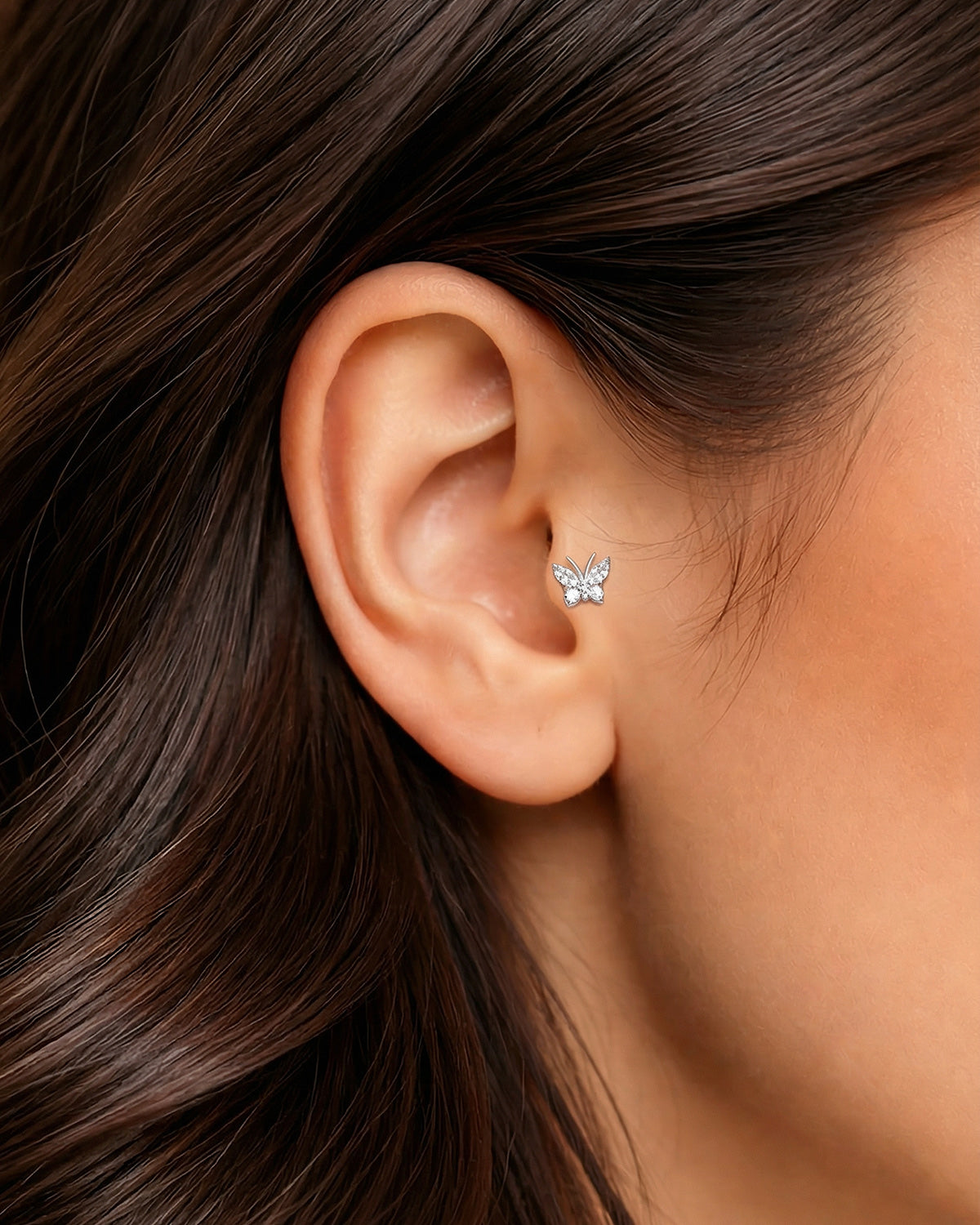 Gümüş renkli zirkon taşlı minimal kelebek piercingin tragus ve helixte duruşu.