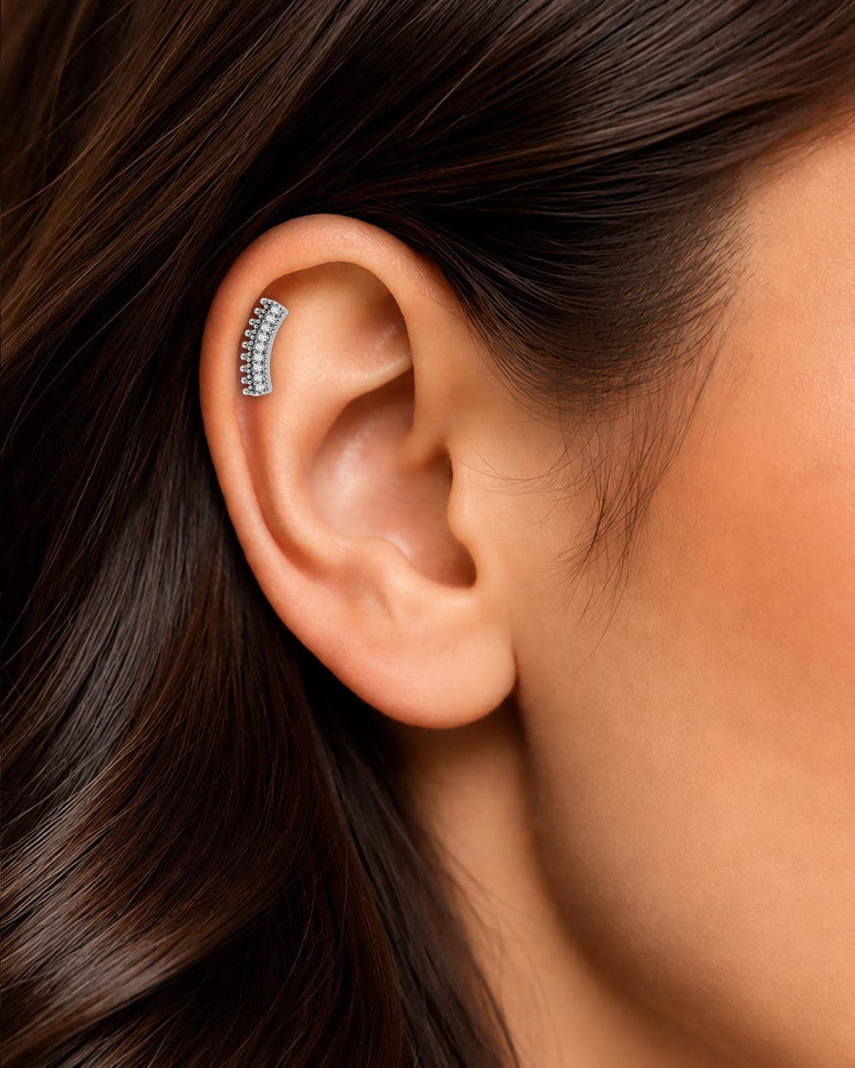 Gümüş renkli kavisli büyük taş figürlü flatback piercingin tragus ve helix bölgesindeki duruşu.